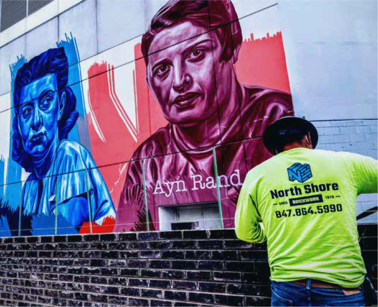 About Us North Shore mason in a hi-vis shirt with the earlier North Shore Brickwork logo, working on a brick wall below a street mural