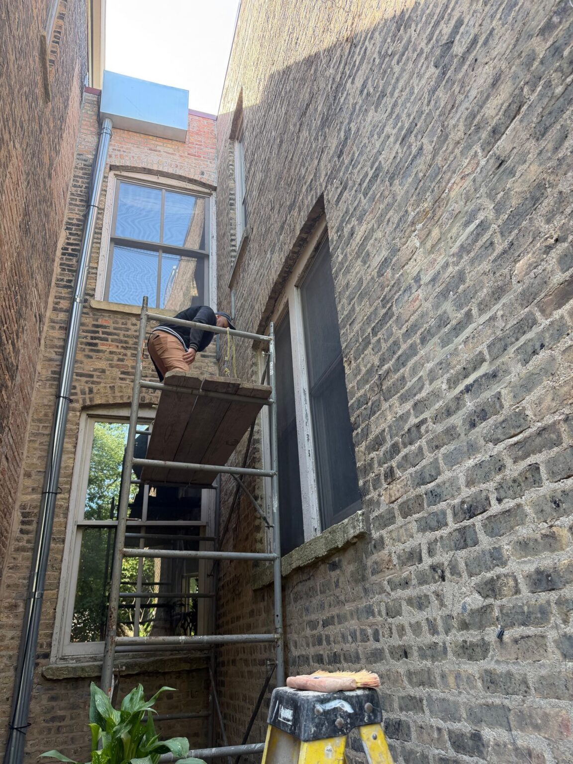 Mason working from a scaffold tower against a common brick wall between two buildings