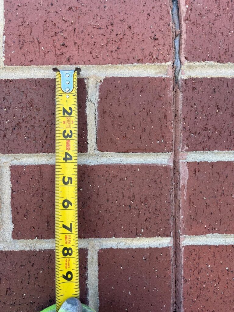Tape measure held against an open vertical mortar joint in a red brick wall